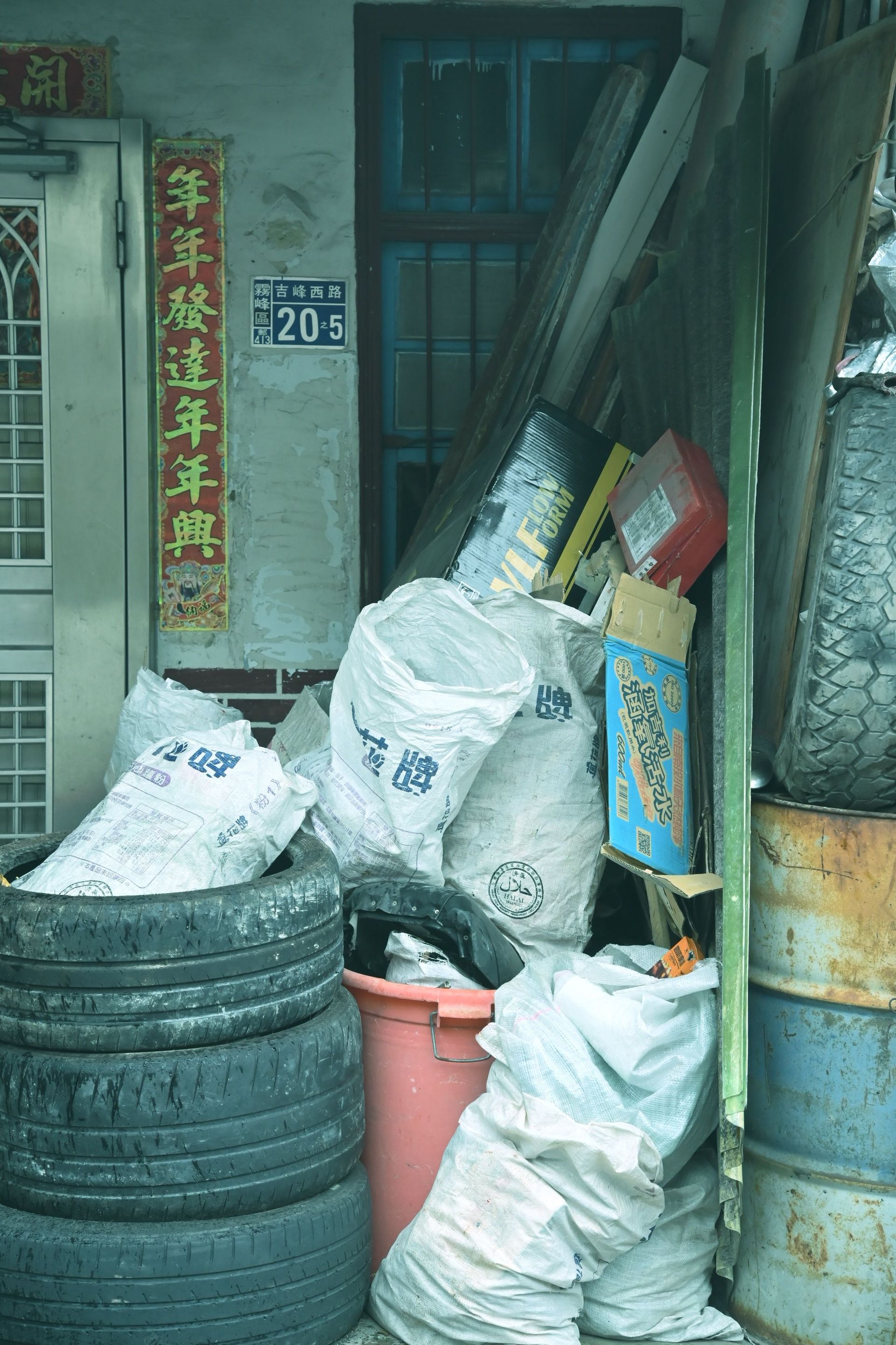 A cluttered corner with tires, trash bags, and discarded items outside a building.
